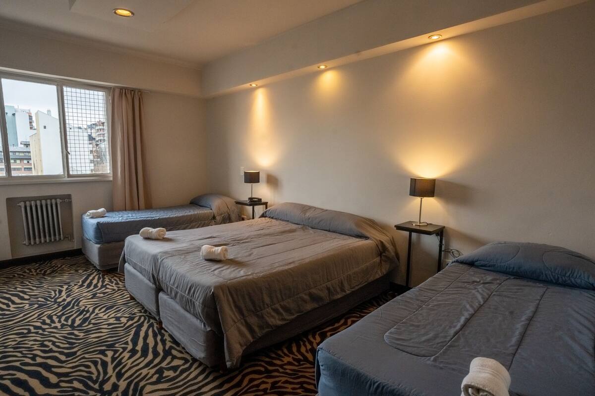 A hotel room with two beds, a zebra-patterned carpet, and a window with a view of buildings.