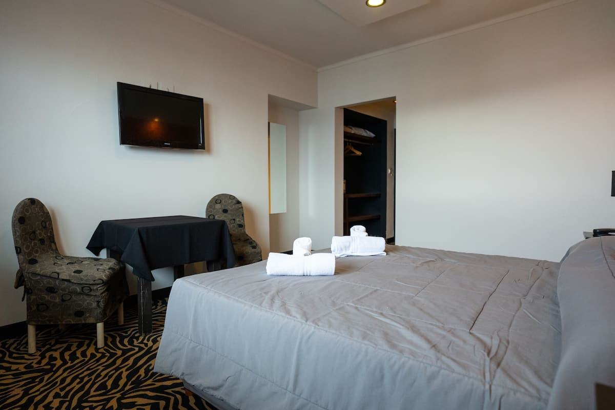 A hotel room with a bed, a TV, a table, two chairs, and a wardrobe.