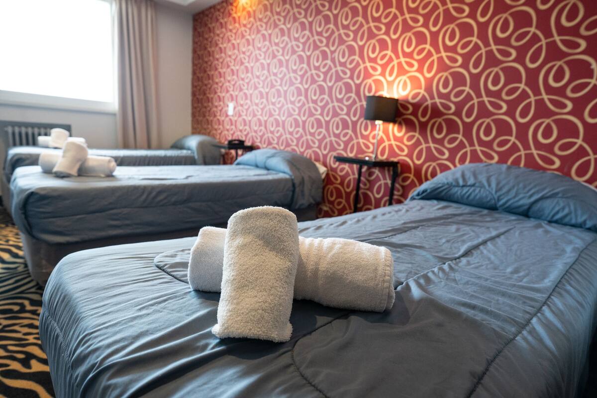 A hotel room with two beds, each with a rolled towel and a lamp on a side table.