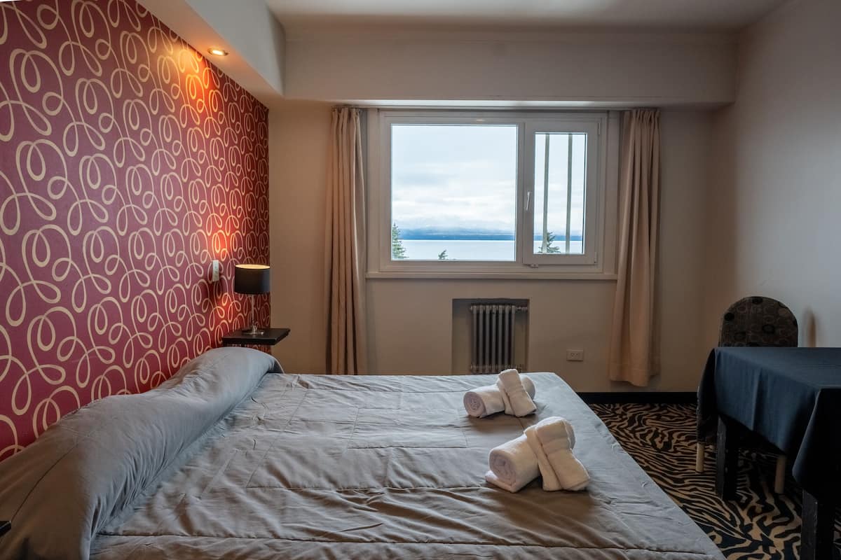 A hotel room with a bed, a window with a view, a radiator, and a table with a tablecloth.