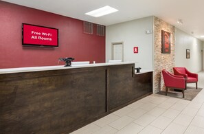 A reception desk with a red wall, a flat-screen TV displaying 'Free Wi-Fi All Rooms', and a stone accent wall with a sign for 'Red Roof Inn'. - Red Roof Inn Temple (Temple)