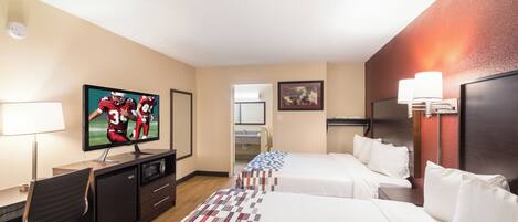 Habitación de hotel con televisión, escritorio, silla, dos camas, lámpara de escritorio y luz en la pared.