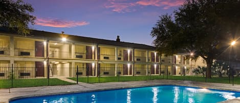 A hotel with a swimming pool, multiple balconies, and a fenced yard.