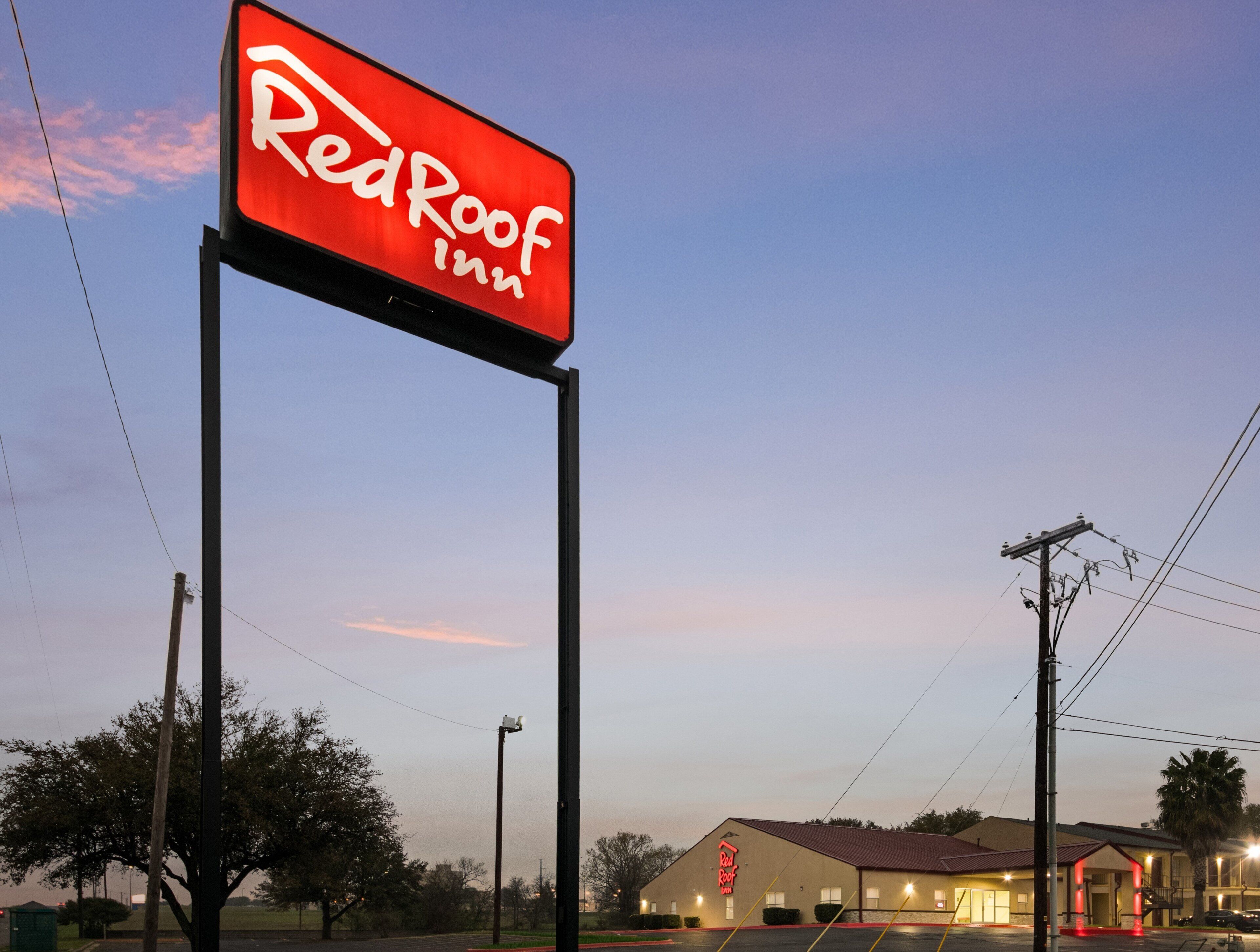 Señal de Red Roof Inn con una vista clara del exterior del edificio, incluyendo su techo y entrada.