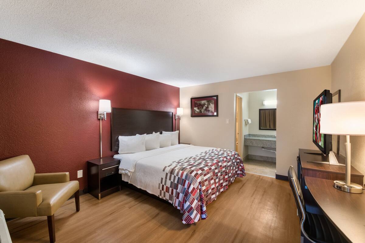 A hotel room with a bed, a chair, a desk with a computer, and a TV.