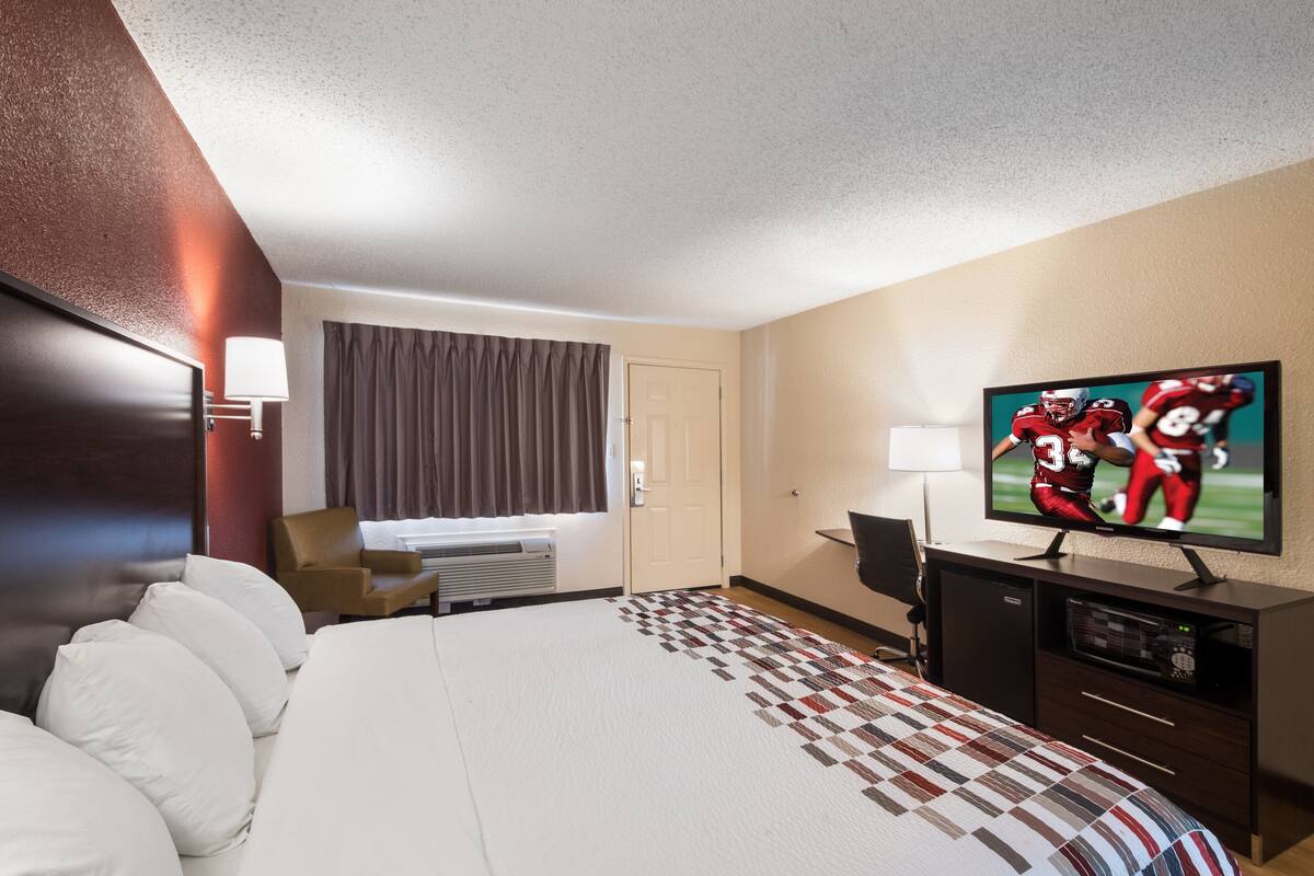 A hotel room with a large bed, a TV on a stand, a desk, and a window with curtains.