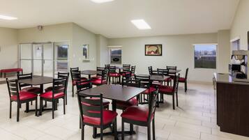 A dining area with multiple tables and chairs, a coffee machine, and a view of the outside through a window.