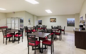 Un espace repas comprenant plusieurs tables et chaises, une machine à café et une vue sur l’extérieur par une fenêtre.
