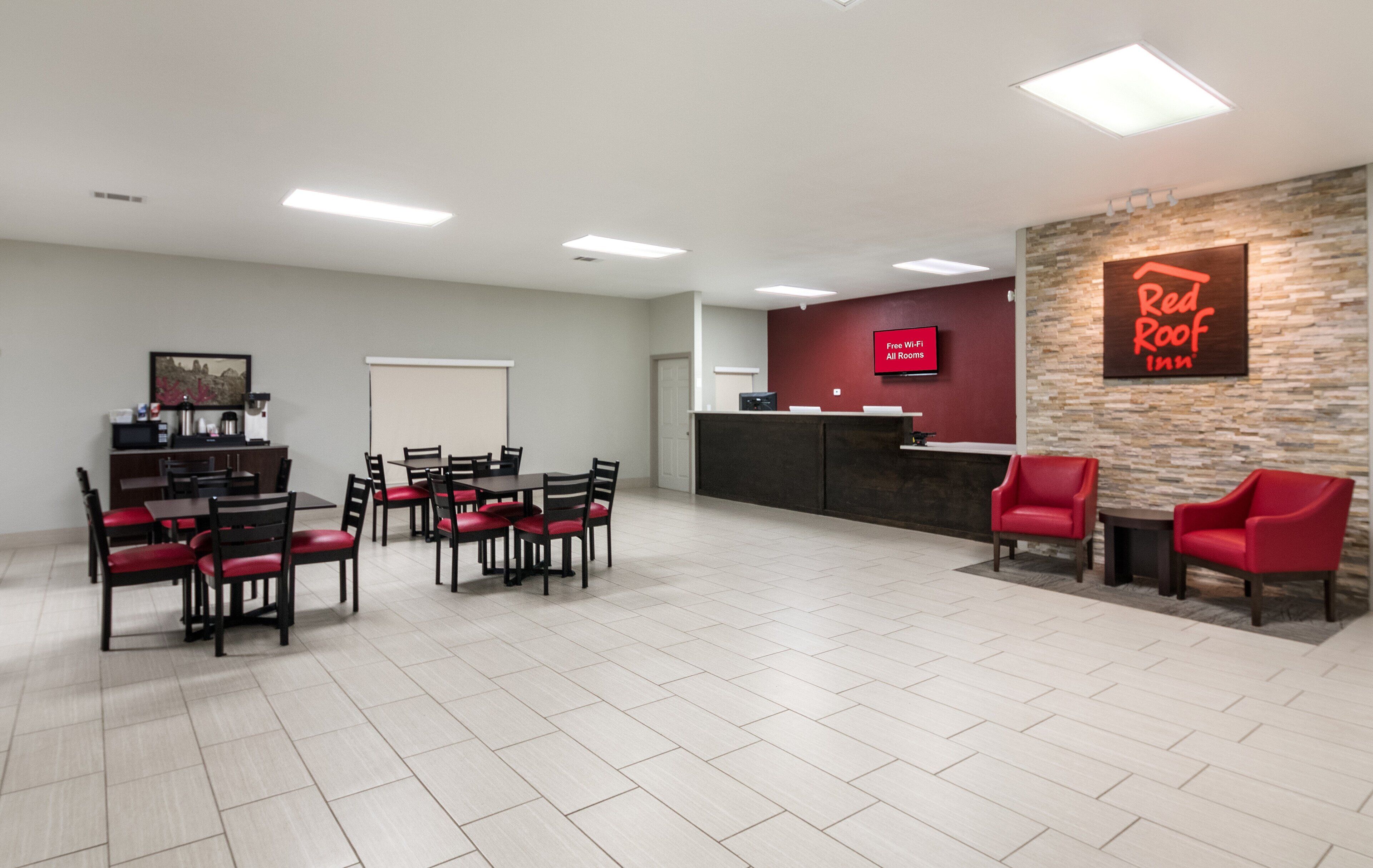 A hotel reception area with a Red Roof Inn sign, a coffee machine, and seating arrangements.