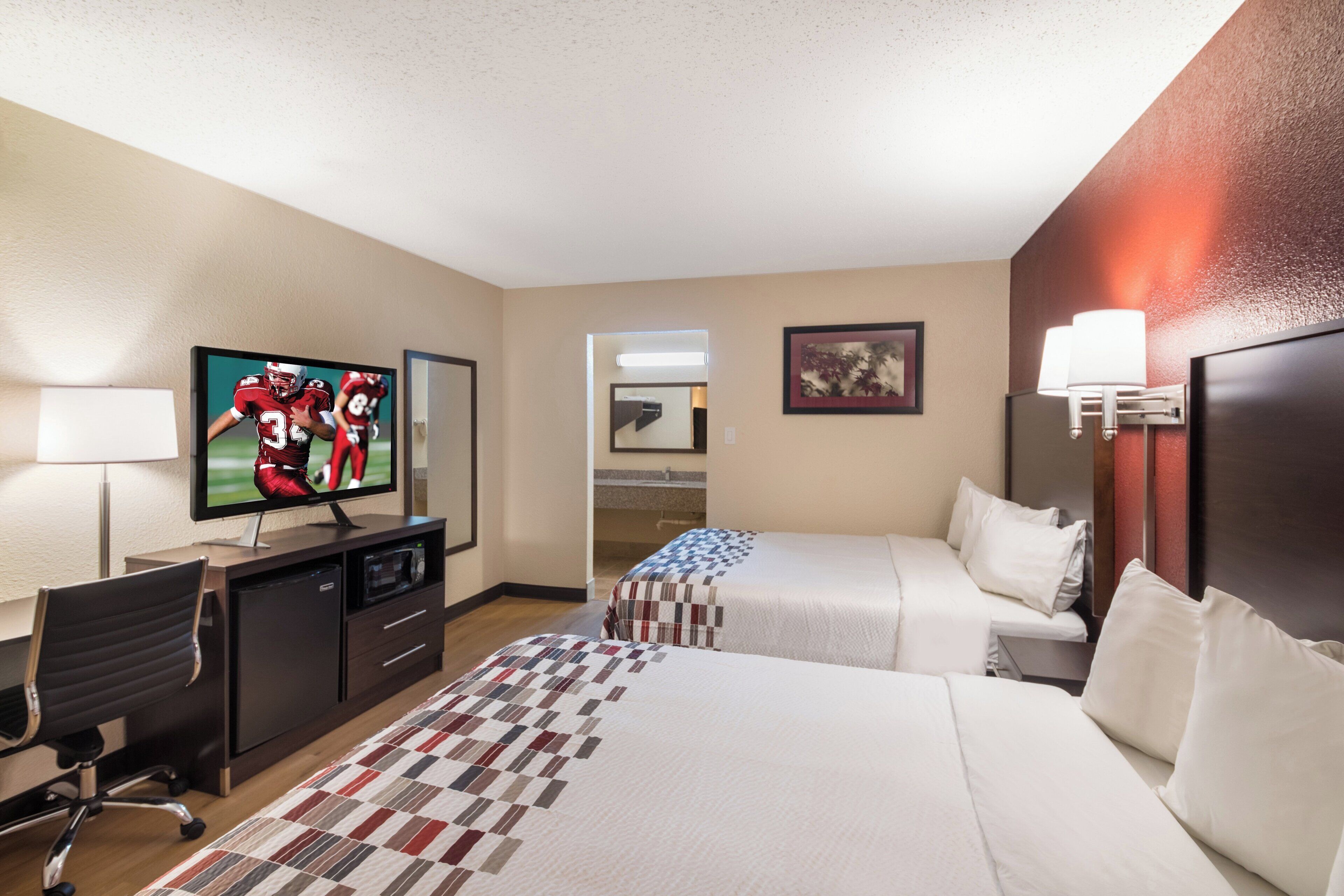 A hotel room with a television, a desk, a chair, two beds, a lamp, and a painting on the wall.