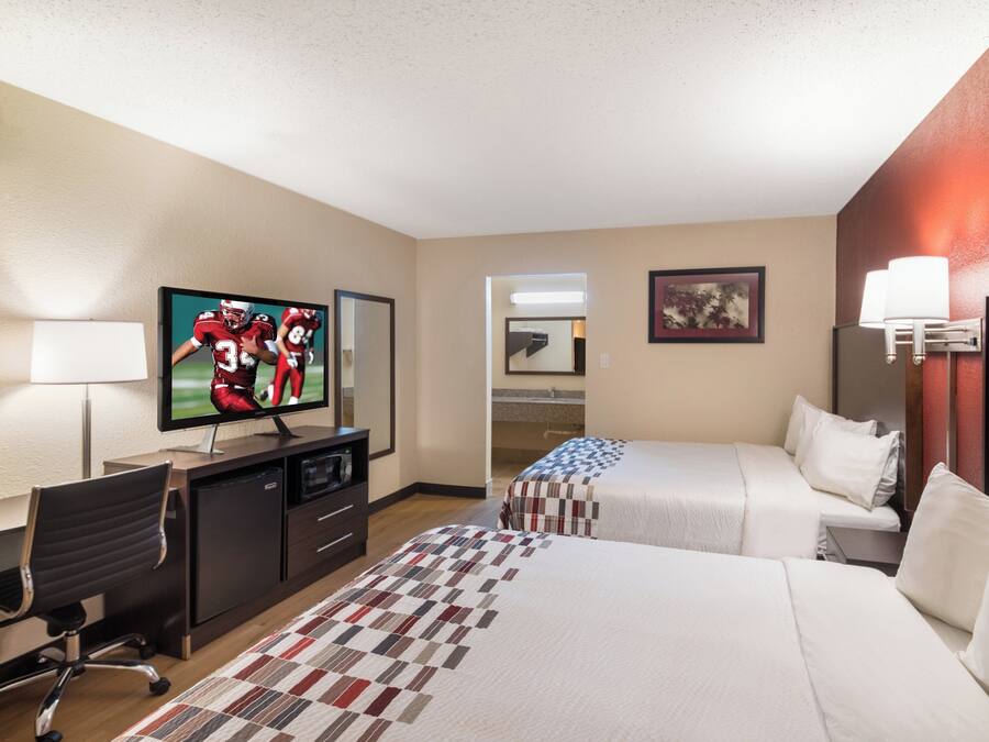 A hotel room with a television, a desk, a chair, two beds, a lamp, and a painting on the wall.