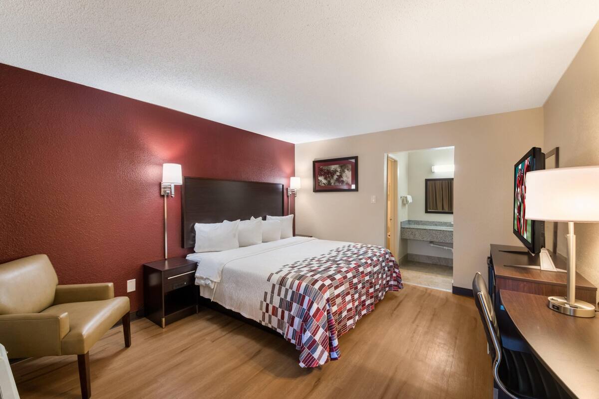 A hotel room with a bed, a desk, a chair, a TV, and a door leading to a staircase.