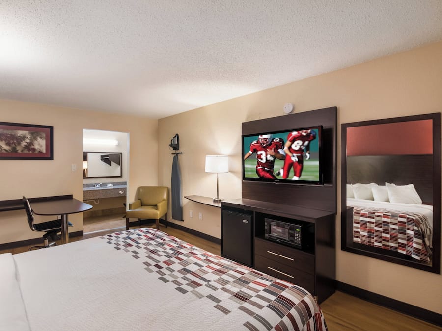 Ein Hotelzimmer mit einem Bett, einem Schreibtisch, einem Sessel, einem Fernseher und einem Spiegel.