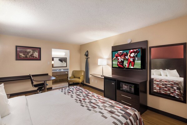 A hotel room with a bed, a desk, a chair, a television, and a mirror.
