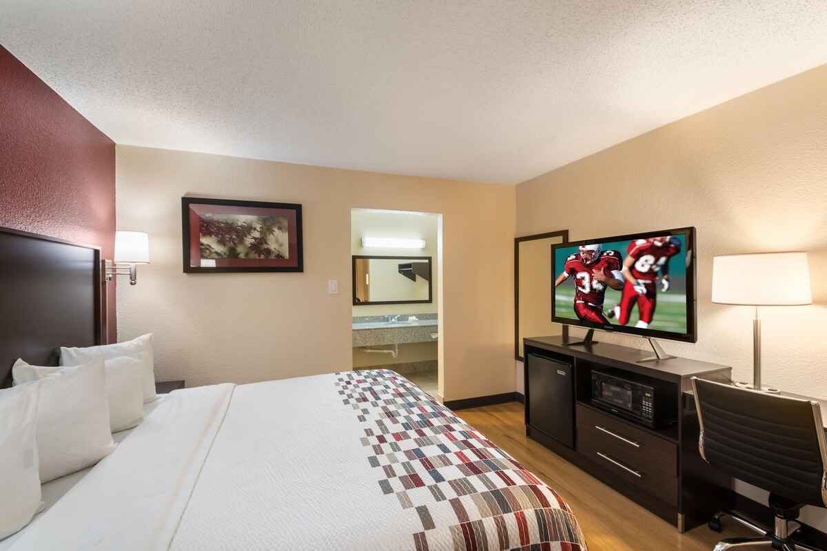 A hotel room with a bed, a desk, a television, and a bathroom visible through an open door.