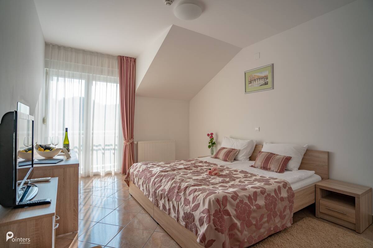 Quarto com cama, mesas de cabeceira, televisão e janela com cortinas.