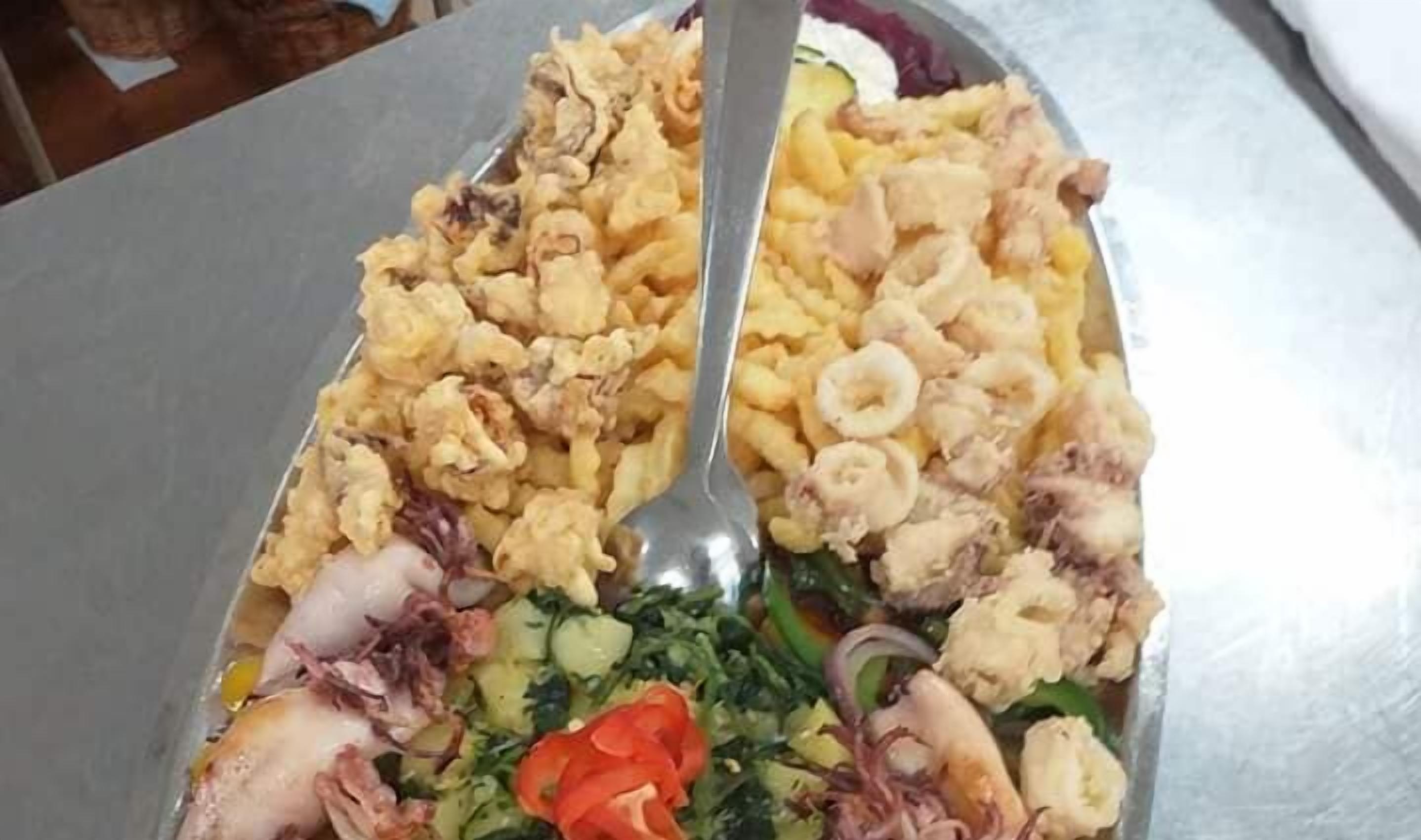A large platter with various seafood items, including fried calamari, shrimp, and possibly some fish, along with some vegetables like tomatoes and greens.