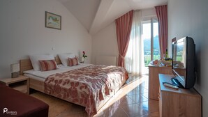 A bedroom with a bed, a desk with a TV, a window with curtains, and a painting on the wall. - Hotel Amarilis (Netretic)