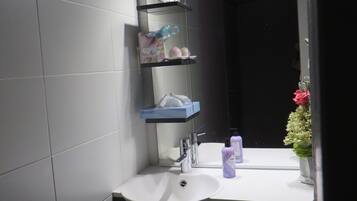 A bathroom with a white sink, a mirror, and shelves holding toiletries.