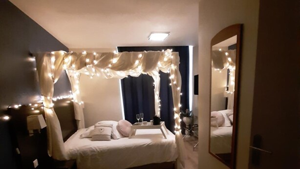 Un dormitorio con cama, mesita de noche, espejo e iluminación decorativa.