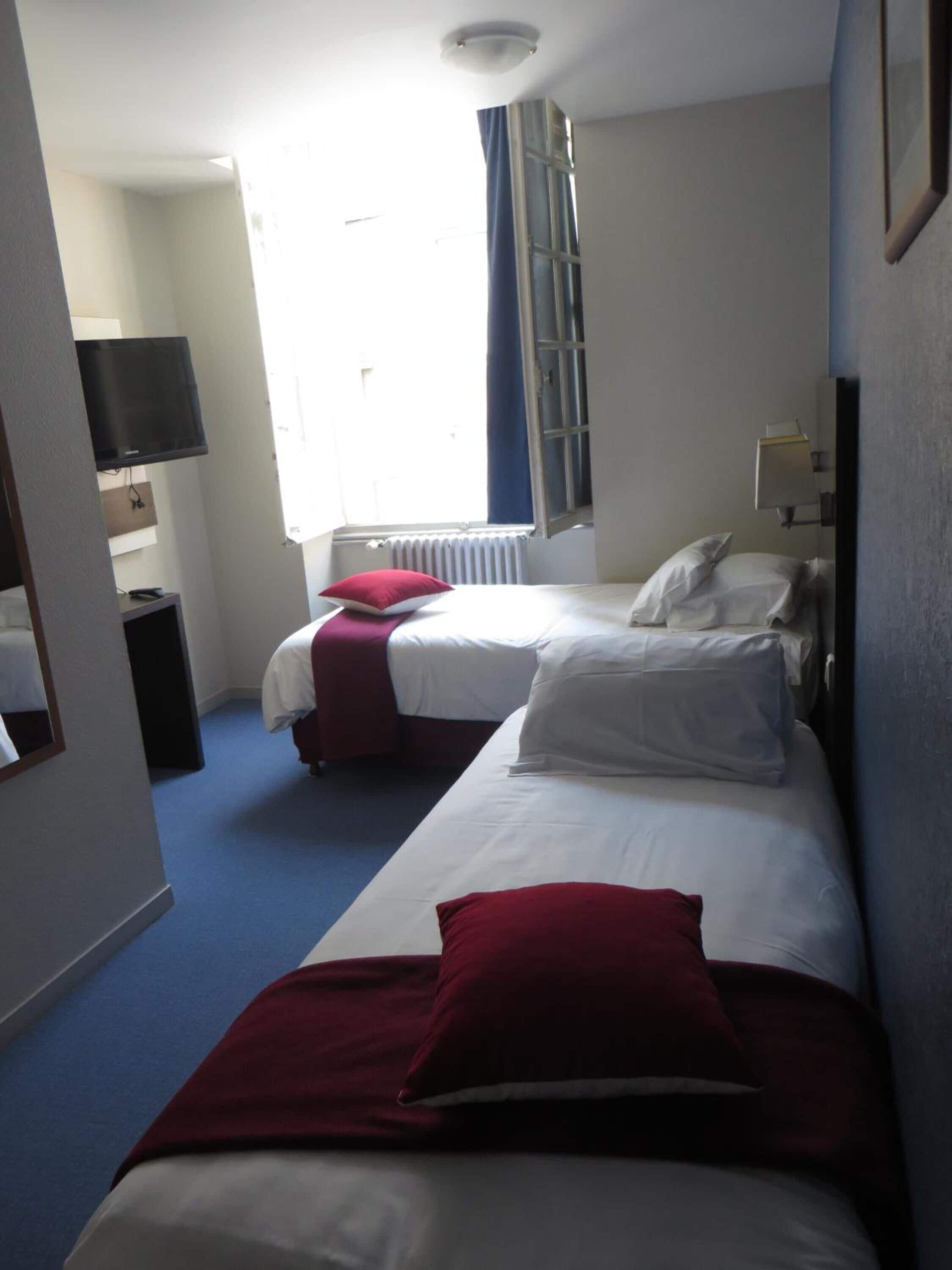 Habitación de hotel con dos camas, televisión, ventana con cortinas y un radiador.