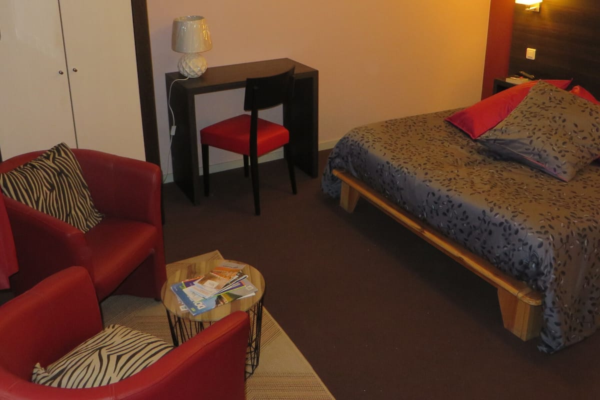 A compact hotel room with a bed, a desk, a chair, and a wardrobe.