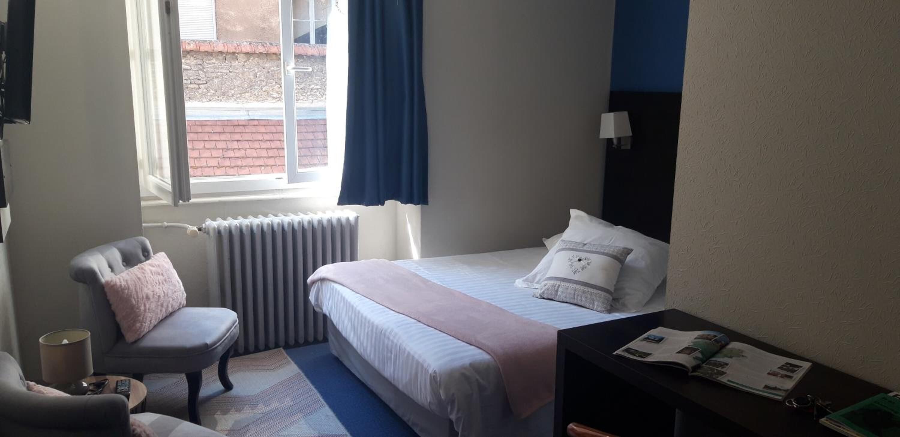 Un dormitorio con cama, una silla, una mesita y un ventanal.
