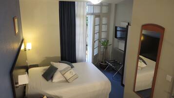 Una habitación de hotel con una cama, un escritorio, una silla, una planta en maceta y un espejo.