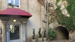 Entrada de un hotel con un toldo rojo con la leyenda "HOTEL REGINA", un arco de piedra y plantas en macetas.