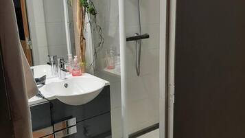 Un baño moderno con lavamanos blanco, armarios oscuros, cabina de ducha de vidrio y un espejo.
