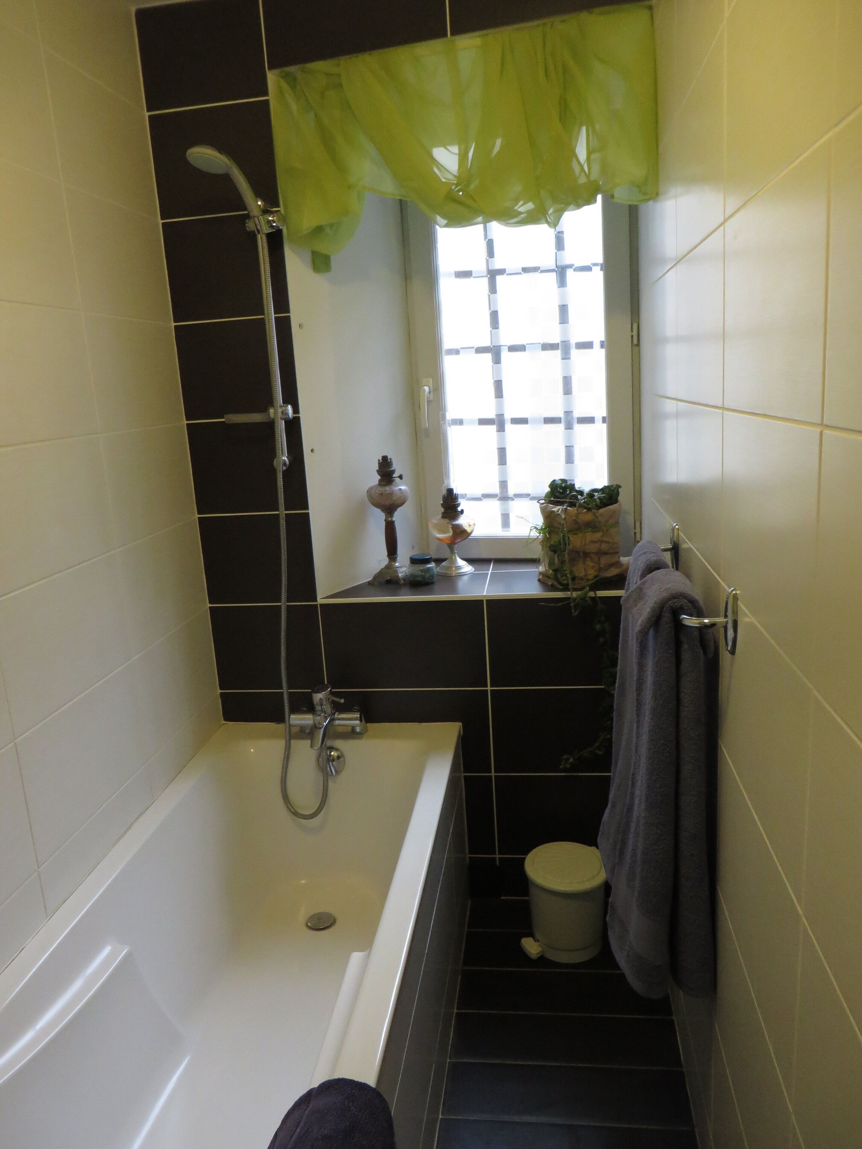 A bathroom with a bathtub, a toilet, and a window with a green curtain.