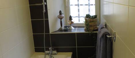 A bathroom with a bathtub, a toilet, and a window with a green curtain.