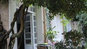 Un patio al aire libre con una mesa y sillas, rodeado de follaje y un edificio con persianas blancas.