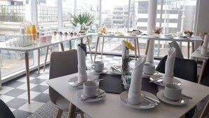 A modern dining area with tables set for breakfast, large windows offering a city view, and a checkered floor pattern. - Fuente Mayor Reñaca (Vina del Mar)