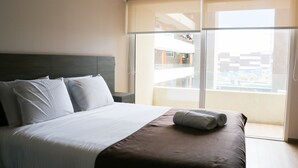 A hotel room with a large bed, a headboard, a window with a view of buildings, and a balcony. - Fuente Mayor Reñaca (Vina del Mar)