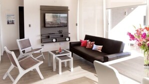 A modern living room with a black sofa, white chairs, a coffee table, and a flat-screen TV mounted on the wall. - Fuente Mayor Reñaca (Vina del Mar)
