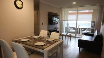 Un comedor con una mesa preparada para cuatro, un televisor de pantalla plana y vistas al mar a través de amplios ventanales.
