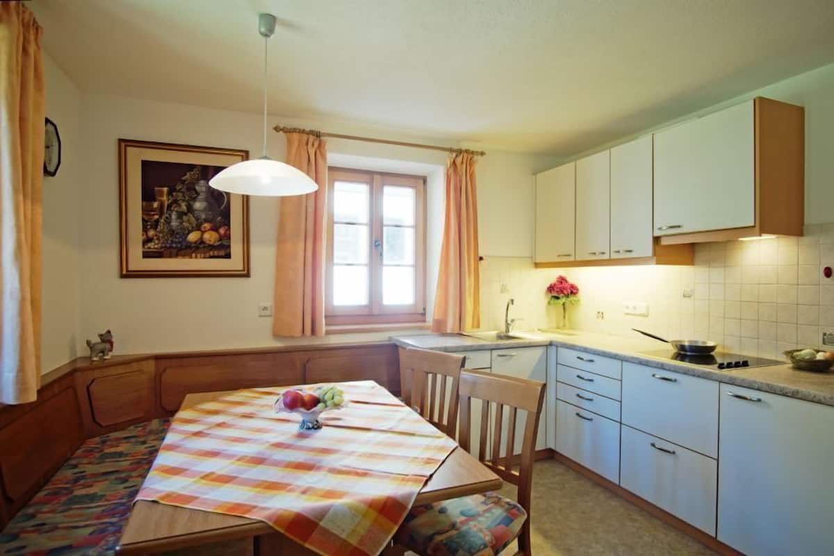A kitchen with a dining table, chairs, a window with curtains, and a sink.