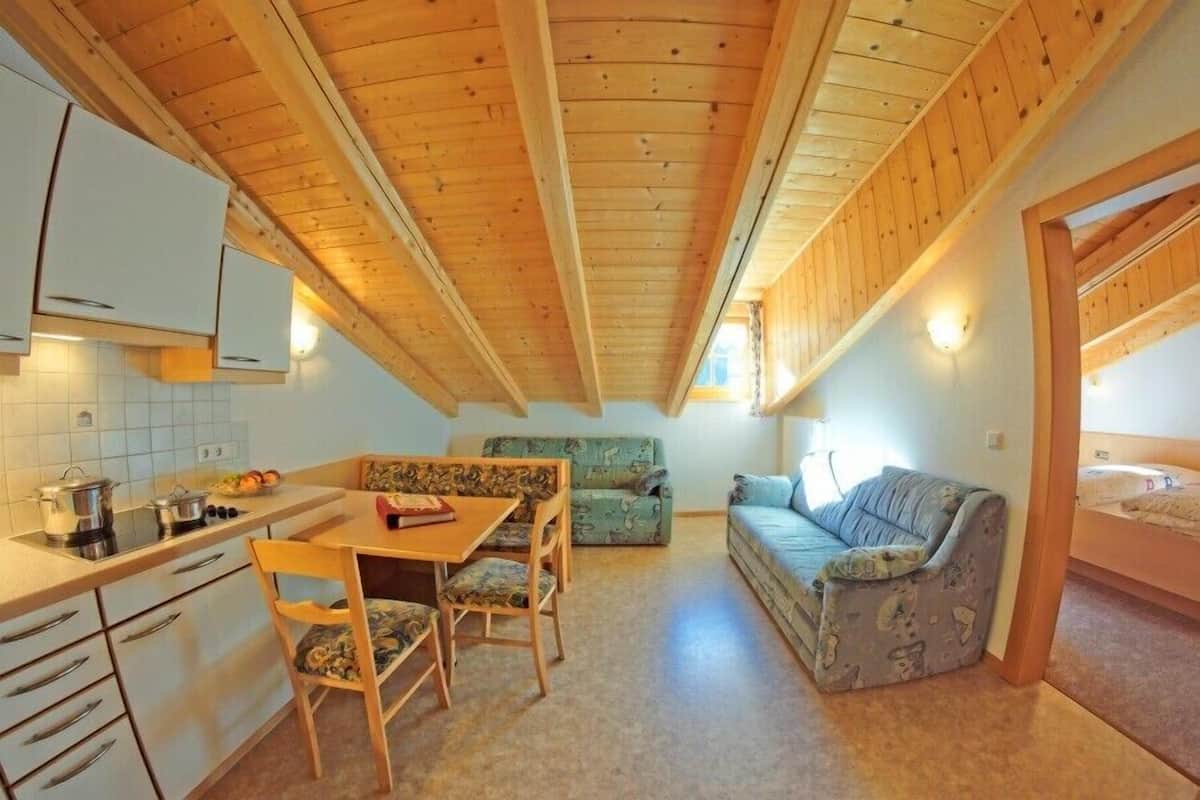 A compact room with a kitchenette, a dining table with chairs, a sofa, and a bed.