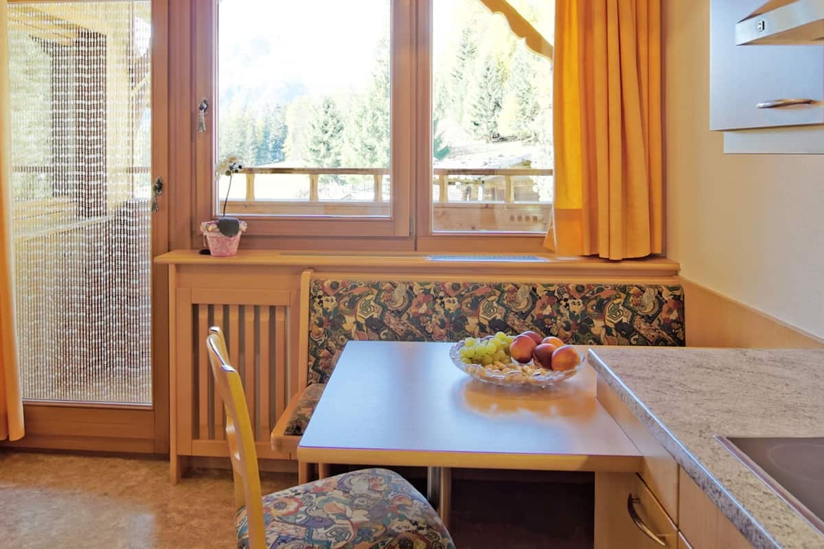 A kitchen with a wooden table, a bowl of fruit, and a window with a view of trees.