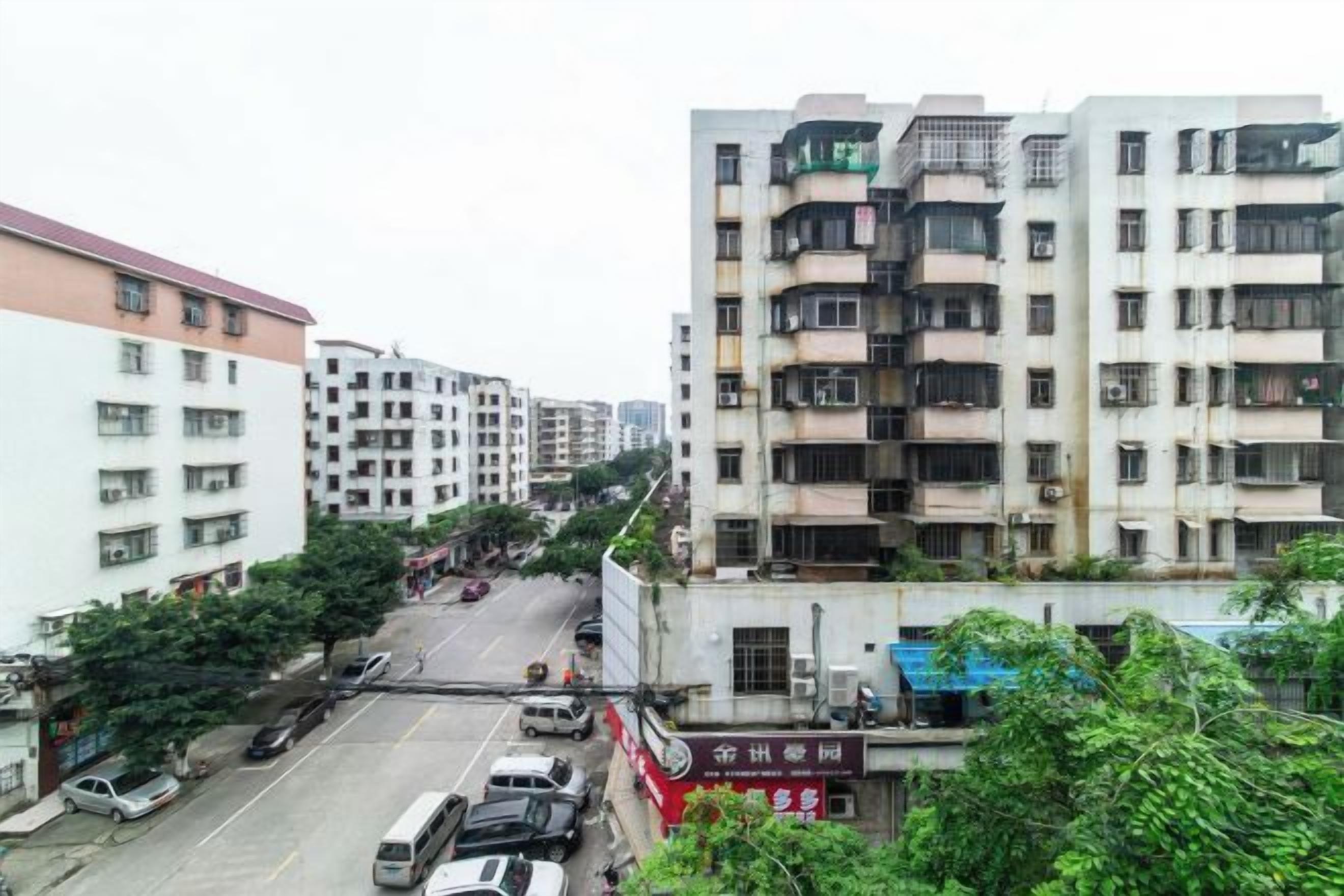 Un edificio residencial de varios pisos con balcones, una calle al frente y coches estacionados.