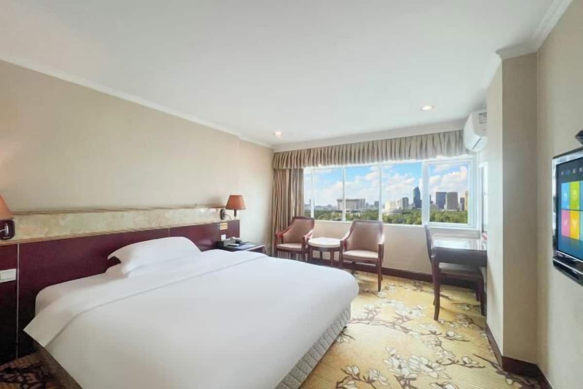 Habitación de hotel con una cama grande, un escritorio con dos sillas, un televisor y una ventana con vista a la ciudad.