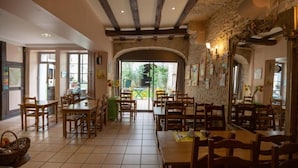 A restaurant with wooden tables and chairs, stone walls, and a view through an arched doorway.
