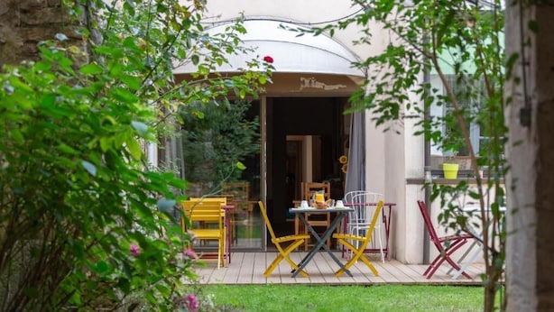 An outdoor seating area with a table and chairs, a glass door entrance, and greenery.