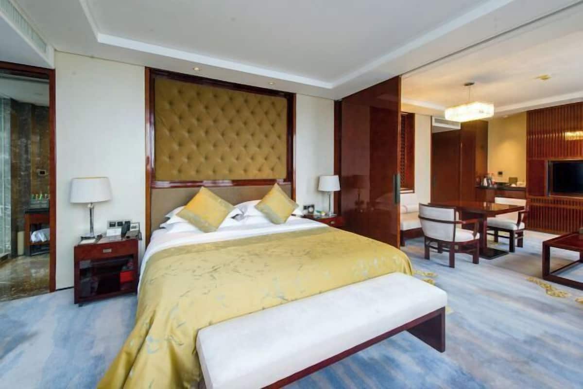 A hotel room with a large bed, a desk, a chair, a television, and a mirror.