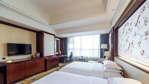 Habitación de hotel con dos camas, televisión, escritorio y un ventanal grande con cortinas.