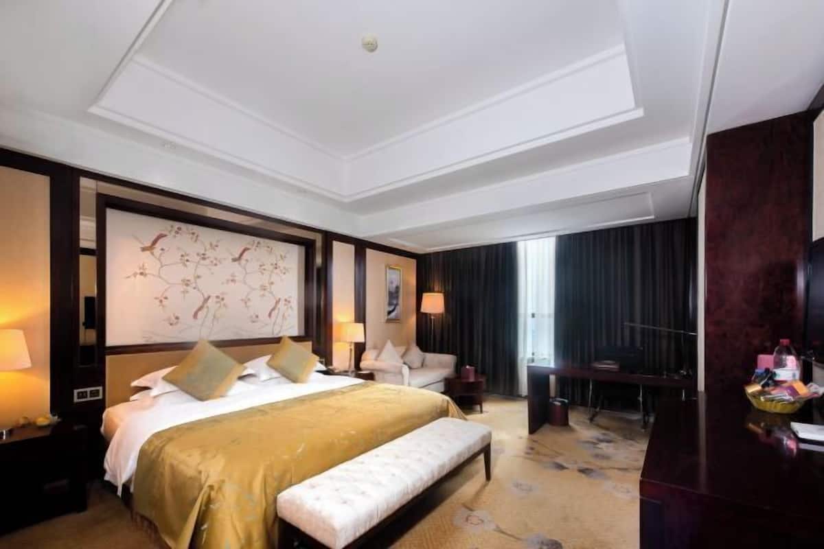 A hotel room with a large bed, a desk, a chair, a bench, and a large window.