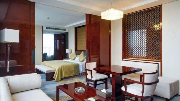Una habitación de hotel con cama, zona de estar con mesa y sillones, sofá y un separador decorativo.