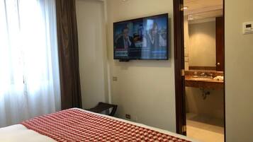 Une chambre d’hôtel avec un lit, un téléviseur fixé au mur et une salle de bain visible à travers une porte ouverte.