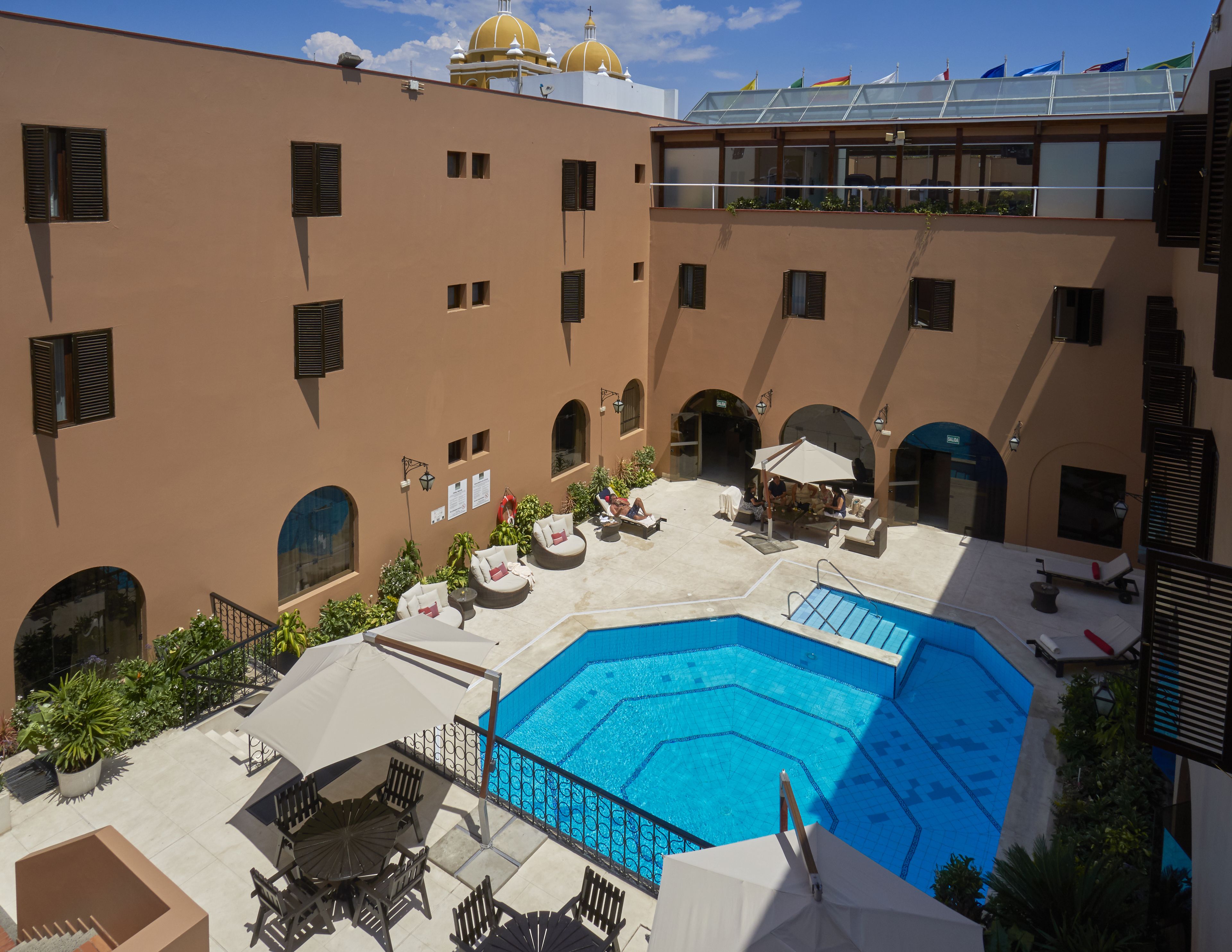 A rooftop pool area with lounge chairs and umbrellas, surrounded by a building with multiple balconies and windows.